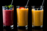 Three colorful fruit smoothies in glasses with metal straws on dark background, healthy breakfast drinks with fresh berries and mint garnish.
