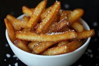 Golden crispy french fries with sea salt in white bowl on dark background. Fast food side dish for restaurants, cafes and food delivery menus.