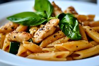 Penne pasta with grilled chicken strips, fresh basil leaves and black pepper in creamy sauce served on white plate, close up view of Italian cuisine.