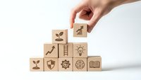 Hand placing wooden cube with growth chart icon on pyramid of business symbol blocks representing strategic planning and development goals.