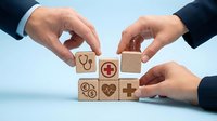 Healthcare professional hands arranging wooden blocks with medical icons including stethoscope, heart, and plus symbol, representing health insurance, wellness planning, and medical services.