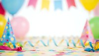 Colorful birthday party background with balloons, confetti, streamers and party hats creating festive celebration atmosphere for events and holidays.