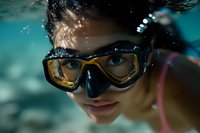 Young woman wearing swimming goggles underwater, close up portrait with teal water and light reflections creating dreamy aquatic atmosphere.