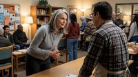 Middle-aged Caucasian woman with gray hair in casual sweater having conversation with African American man in plaid shirt at community center meeting.