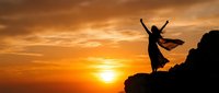 Woman silhouette dancing on mountain cliff at golden sunset with flowing dress and raised arms celebrating freedom and joy in nature landscape.