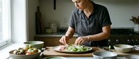 Young Caucasian man in gray shirt preparing fresh salad in modern kitchen, healthy cooking and meal preparation at home for lifestyle content.