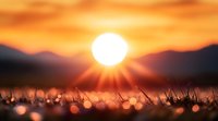 Dramatic sunrise over mountain silhouettes with glowing sun and dewy grass in foreground creating magical bokeh effect at dawn. Nature awakening moment.
