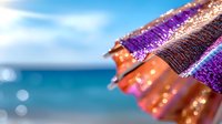 Colorful beach umbrella with glitter sparkles against blurred tropical ocean background, creating dreamy summer atmosphere with bokeh effect and soft focus.