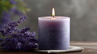 Glowing purple ombre candle with burning flame next to fresh lavender sprigs on rustic wooden surface, creating peaceful spa atmosphere for relaxation and aromatherapy.