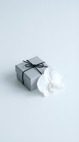 Elegant gray gift box with black ribbon bow and white orchid flower on clean white background for special occasions and celebrations.
