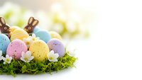 Colorful speckled Easter eggs in pastel shades with chocolate bunny silhouettes nestled in green moss on white background for spring holiday celebrations.