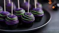 Dark chocolate cake pops decorated with purple and green stripes, topped with sparkling sugar sprinkles on black plate against dark background with bokeh lights.