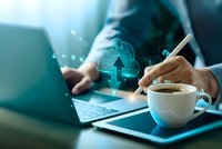 Businessman working on laptop with digital cloud computing icons and coffee cup on modern desk in office environment for technology concepts.
