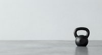 Black kettlebell on wooden floor against white wall in minimalist gym setting for fitness and strength training workouts.