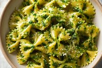 Farfalle pasta with fresh pesto sauce and grated parmesan cheese in ceramic bowl, homemade Italian cuisine.
