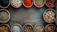 Aromatic spices and herbs in rustic wooden bowls arranged on weathered turquoise wooden background, creating frame with copy space for text in center.