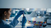 Female scientist in blue gloves examining test tube sample in modern laboratory with colorful vials for medical research and pharmaceutical development.