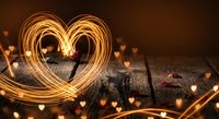 Glowing heart shape made with sparkler light trails on rustic wooden background with warm bokeh hearts for romantic celebrations and love concepts.