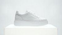 White platform sneaker displayed on a white pedestal against a light background, showcasing minimalist footwear design for fashion and retail.