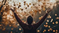 Person with raised arms celebrating as golden coins fall from above against warm sunset bokeh background.