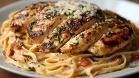 Grilled chicken breast sliced and served over creamy fettuccine pasta with tomatoes, herbs and parmesan cheese on white plate, close up view of Italian cuisine.
