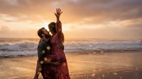 Happy couple dancing on beach at sunset with golden sky and ocean waves creating romantic atmosphere for vacation memories.