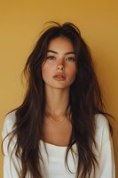Young Asian woman with long dark hair wearing white top and gold necklace against warm yellow background, natural makeup look emphasizing full lips and glowing skin.