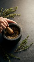 Woman grinding herbs and spices in stone mortar with wooden pestle on dark slate surface surrounded by fresh thyme sprigs for cooking and seasoning.