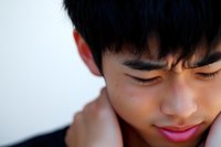 Close up portrait of young Asian male with eyes closed and gentle smile showing peaceful, serene expression against light background.