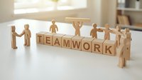 Wooden figures holding hands and standing around blocks spelling teamwork on white surface, representing collaboration, unity, and cooperative business success.