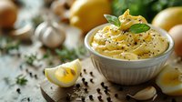 Creamy homemade mayonnaise sauce with fresh herbs, black pepper, lemon and garlic in ceramic bowl on rustic wooden table, selective focus.