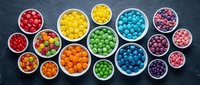 Colorful candy assortment in white bowls on dark slate background. Rainbow sweets collection for confectionery, party planning and dessert concepts.