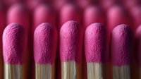Pink lipsticks in row showing textured matte finish on golden tubes, macro beauty photography with selective focus and soft lighting effect.