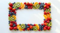 Fresh colorful fruit frame with strawberries, blueberries, kiwi and orange slices on white background. Healthy eating border for menu design.