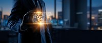 Businessman in suit holding glowing gear icon with digital interface against blurred city skyline at dusk, representing technology, innovation, and business solutions.