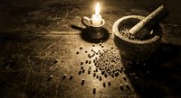 Stone mortar and pestle with scattered peppercorns on rustic wooden table, lit by candlelight, evoking ancient herbal apothecary atmosphere.