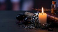 Mystical witchcraft altar with burning candle, pentagram, crystals, herbs and ritual tools creating atmospheric occult scene for spiritual practices.