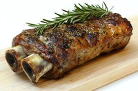 Grilled lamb shank with fresh rosemary sprig on wooden cutting board, showing caramelized crust and juicy meat texture. Close up food photography for restaurant menu.