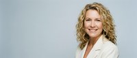 Professional middle-aged Caucasian businesswoman with curly blonde hair smiling confidently in cream blazer against neutral background for corporate use.
