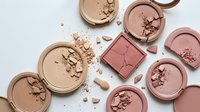 Broken makeup powder compacts in nude and pink shades scattered on white background. Cosmetic products for beauty and fashion industry applications.