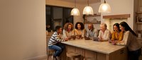 Diverse group of people gathered around kitchen island during evening social gathering, enjoying conversation and connection in warm home setting.