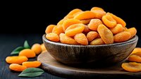 Fresh dried apricots in wooden bowl on dark background with green leaves, healthy organic snack for natural food photography and packaging design.