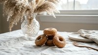 Freshly baked homemade donuts with sugar coating arranged on white linen tablecloth near window with natural light and dried pampas grass decoration.