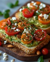 Avocado toast topped with cherry tomatoes, feta cheese, almonds and herbs on seeded bread served on wooden cutting board. Fresh healthy breakfast.