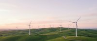 Aerial view of wind turbines scattered across rolling green hills during golden hour sunset, showcasing renewable energy infrastructure and sustainable power generation landscape.