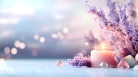 Romantic spa composition with glowing candle in glass jar, purple lilac flowers and rose quartz crystals against blurred bokeh background.