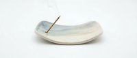 Ceramic incense holder with curved dish design and metal stick rest, isolated on white background for home decor and aromatherapy product use.