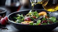 Fresh salad with olive oil pouring from bottle, mixed greens, boiled eggs, and cranberries in dark bowl against black background, dramatic food photography.