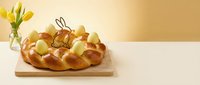 Traditional braided Easter bread with colorful eggs on wooden board, spring holiday baking celebration with tulips in background for festive design.