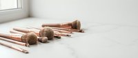 Rose gold makeup brushes set with natural bristles on white marble surface for beauty and cosmetics application in bright minimalist setting.
